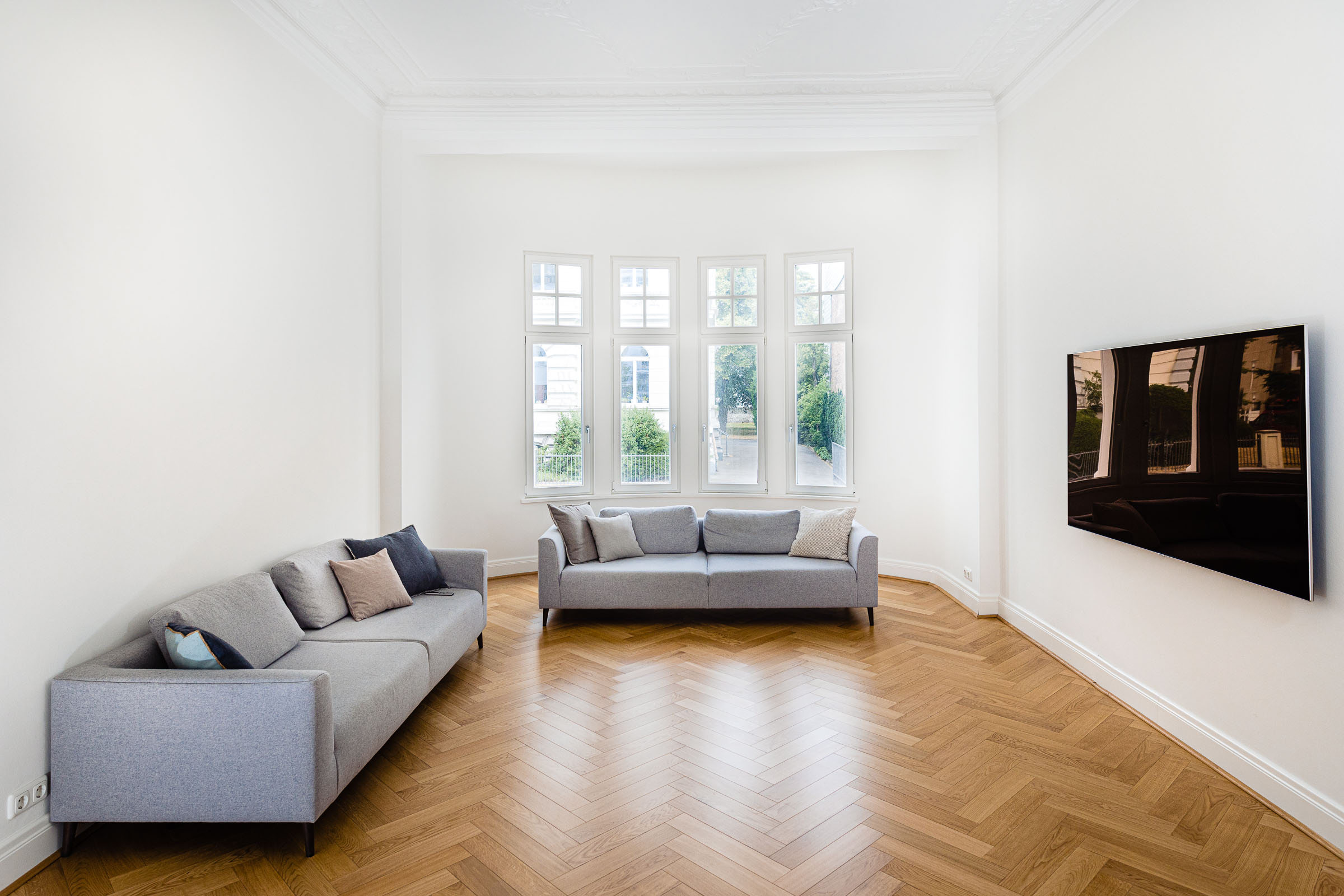 Das Wohnzimmer einer Luxusimmobilie mit braunem Parkettboden und lichtdurchfluteten Räumen.